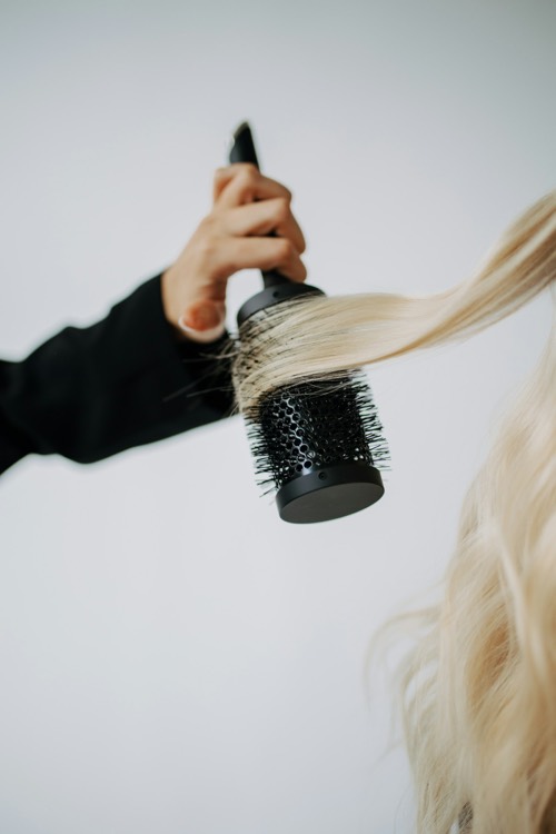 Hand föhnt langes blondes Haar über eine Rundbürste