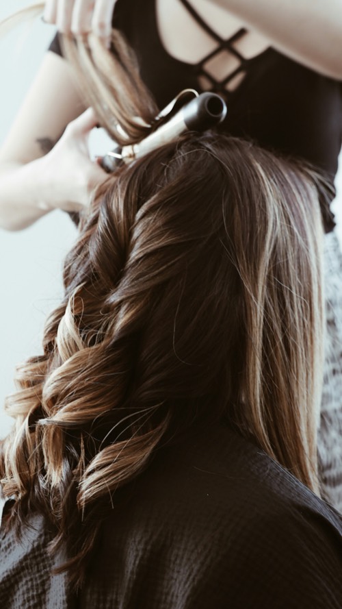 Langes, braunes Haar wird von hinten mit dem Lockenstab in Wellen gelegt