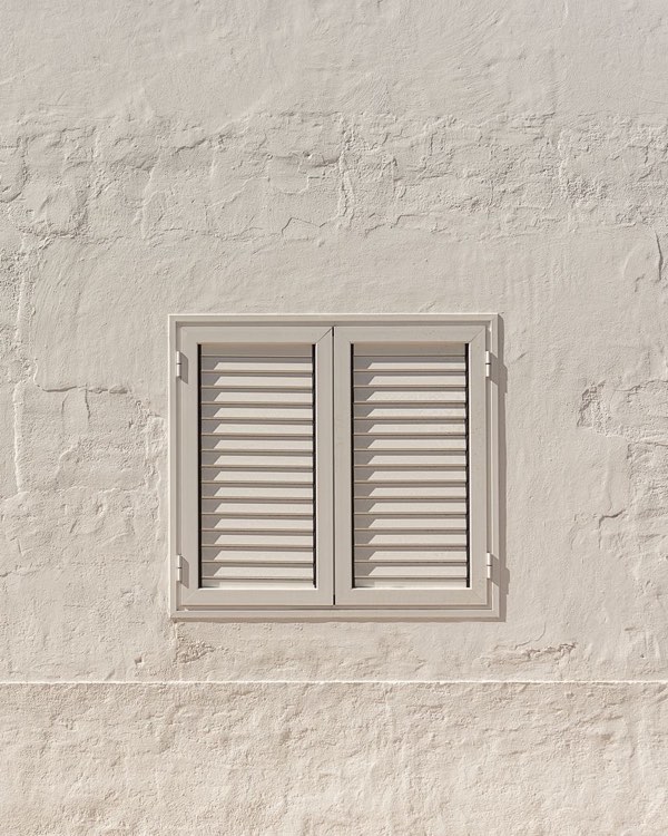 Hell gestrichene verputzte Hauswand mit grau lackiertem Fensterladen mit Lamellen