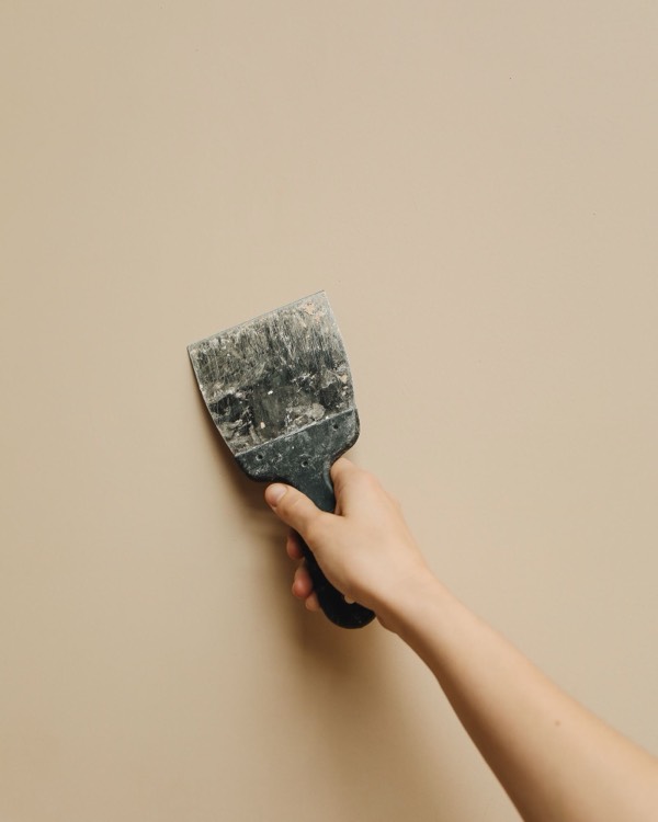 Junge Hand hält einen Spachtel an eine helle Wand
